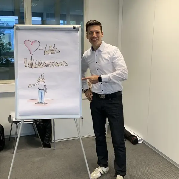 Jörg Vogelgesang zeigt lachend auf ein Willkommens-Flipchart zum Trainingsstart