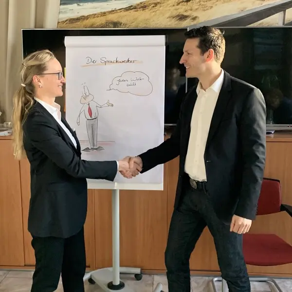 Jörg Vogelgesang gibt einer Teilnehmerin am Flipchart die Hand